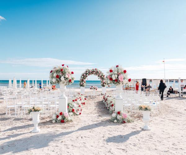 Beach wedding with floral decorations and white chairs.