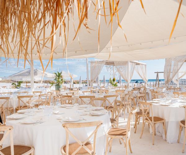 Elegant outdoor setup with white tables and wooden chairs on the beach.