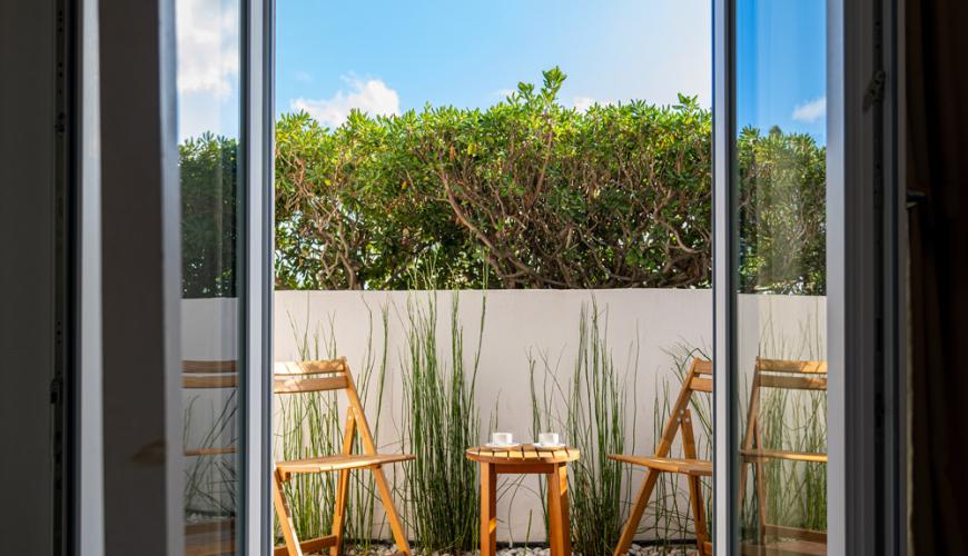 Balcon avec chaises et table, vue sur haie verte.