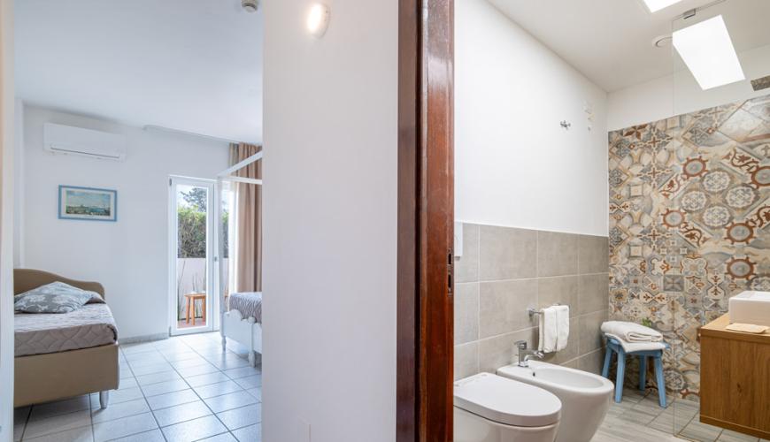 Chambre lumineuse avec salle de bain moderne et balcon.